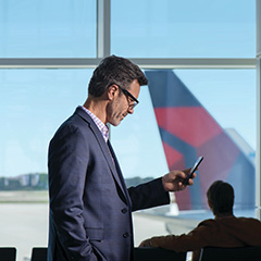Business man in airport using phone with Delta tail in background